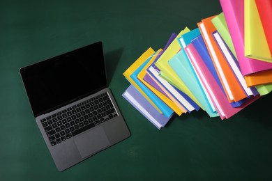 Photo of Stack of many colorful books and laptop on green background, above view