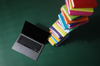 Photo of Stack of many colorful books and laptop on green background, above view