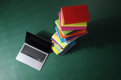 Photo of Stack of many colorful books and laptop on green background, flat lay