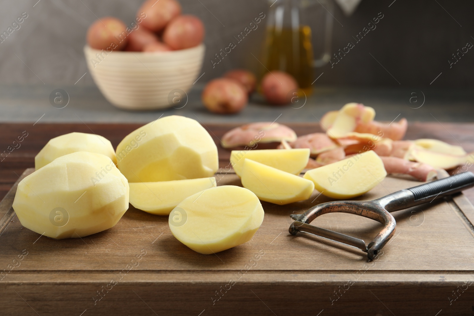 Photo of Fresh raw potatoes, peels and peeler on table