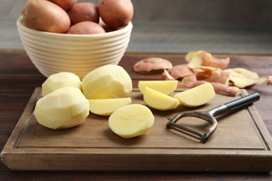 Fresh raw potatoes, peels and peeler on wooden table