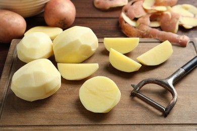 Fresh raw potatoes, peels and peeler on wooden table