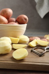 Photo of Fresh raw potatoes and peeler on table