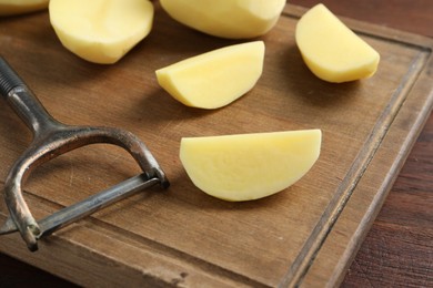 Photo of Fresh raw potatoes and peeler on wooden table