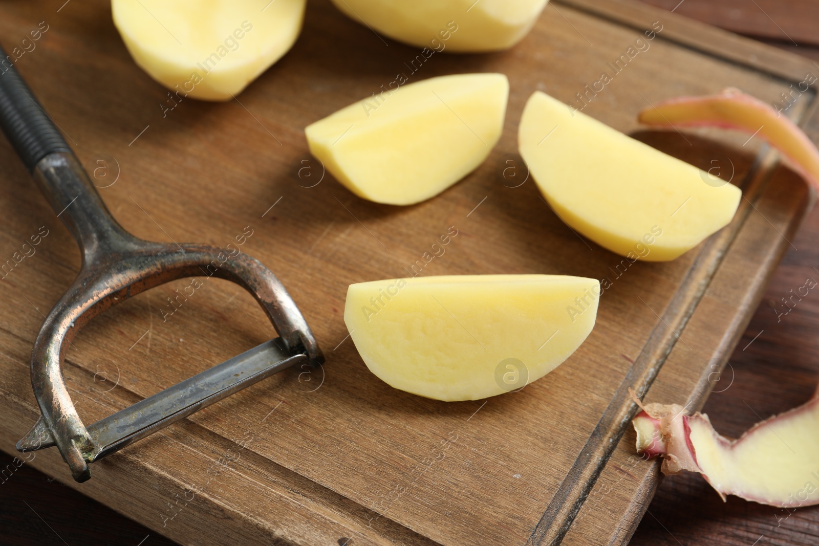 Photo of Fresh raw potatoes, peels and peeler on wooden table