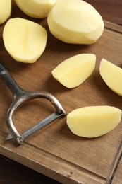 Photo of Fresh raw potatoes and peeler on table