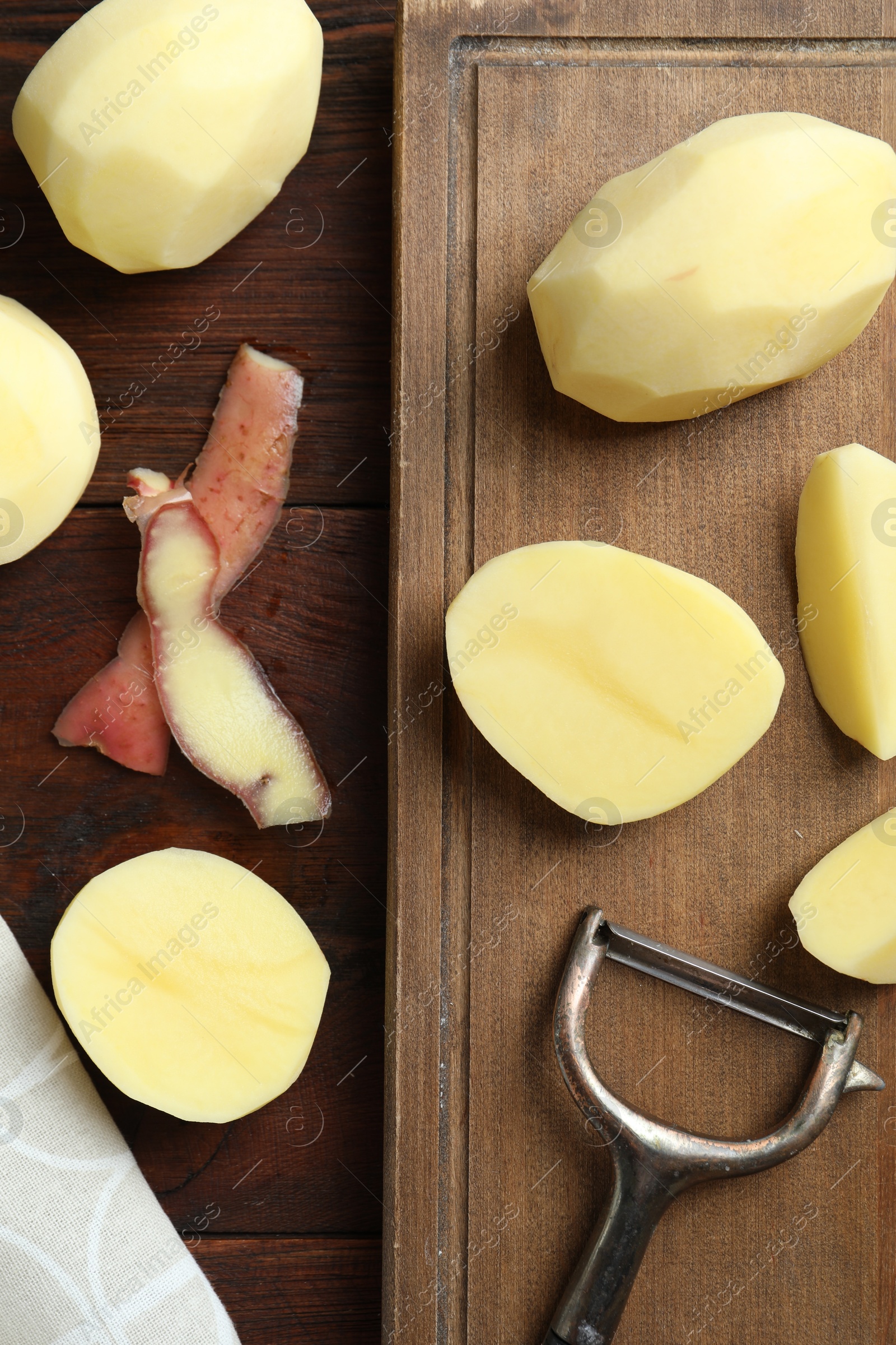 Photo of Fresh raw potatoes, peels and peeler on wooden table, top view