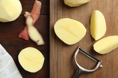 Photo of Fresh raw potatoes, peels and peeler on wooden table, top view