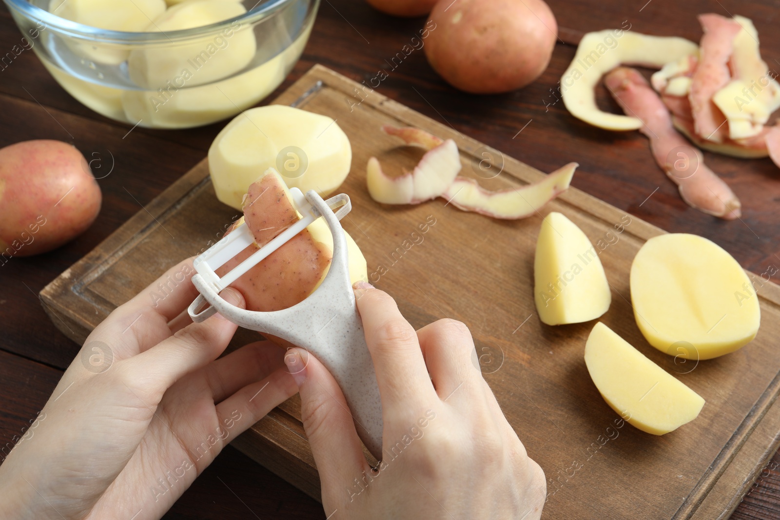 Photo of Woman peeling fresh potato with peeler at wooden table