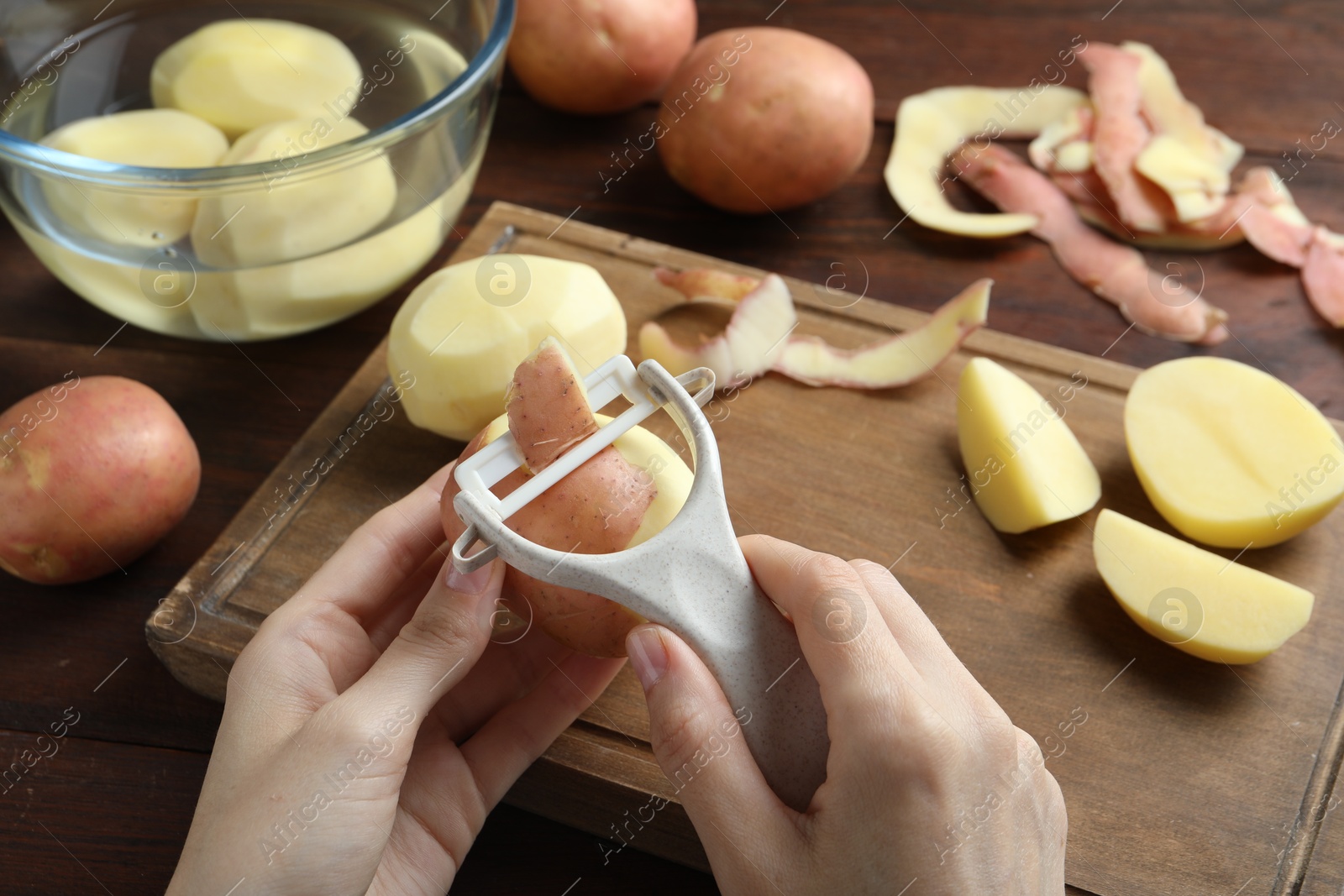 Photo of Woman peeling fresh potato with peeler at wooden table