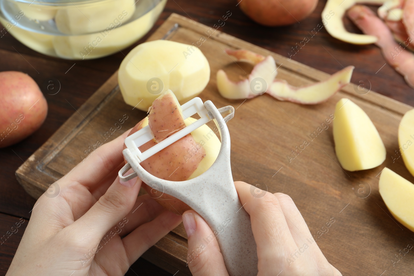 Photo of Woman peeling fresh potato with peeler at wooden table