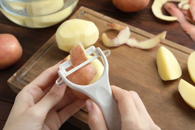 Woman peeling fresh potato with peeler at wooden table