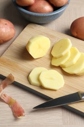 Photo of Fresh raw potatoes, peels and knife on wooden table