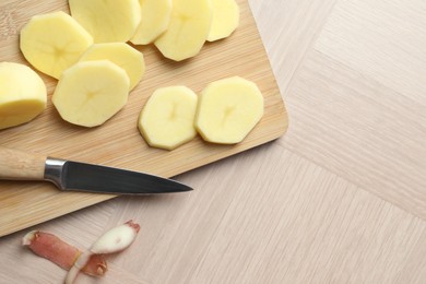 Photo of Fresh raw potatoes, peels and knife on wooden table, top view. Space for text