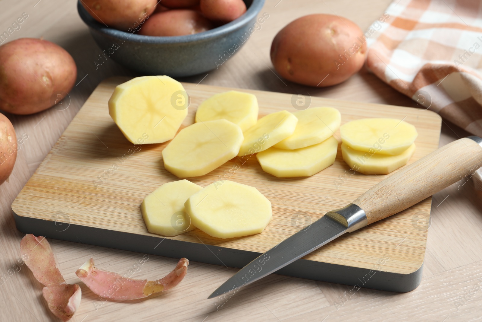 Photo of Fresh raw potatoes, peels and knife on wooden table