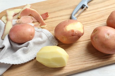 Fresh raw potatoes, peels and peeler on white table