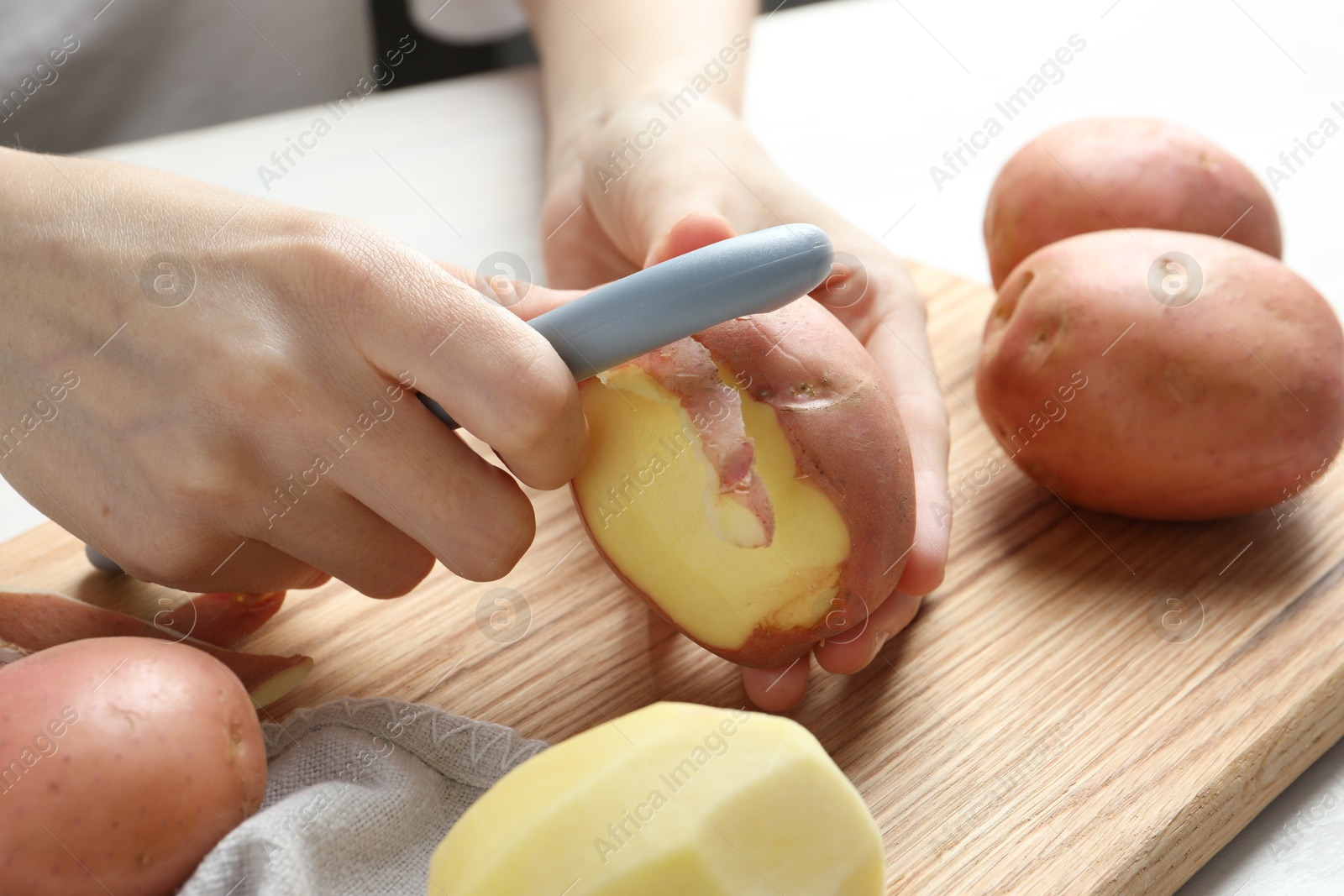 Photo of Woman peeling fresh potato with peeler at table, closeup