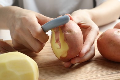 Photo of Woman peeling fresh potato with peeler at table, closeup