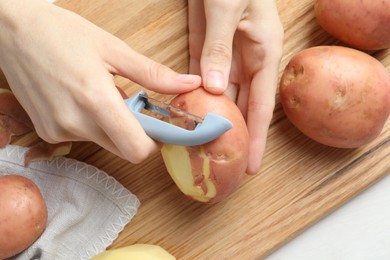 Woman peeling fresh potato with peeler at table, top view