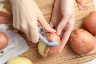 Photo of Woman peeling fresh potato with peeler at table, top view