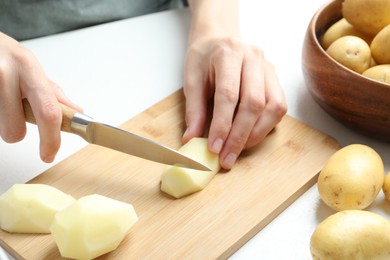 Photo of Woman cutting raw potato at white table, closeup