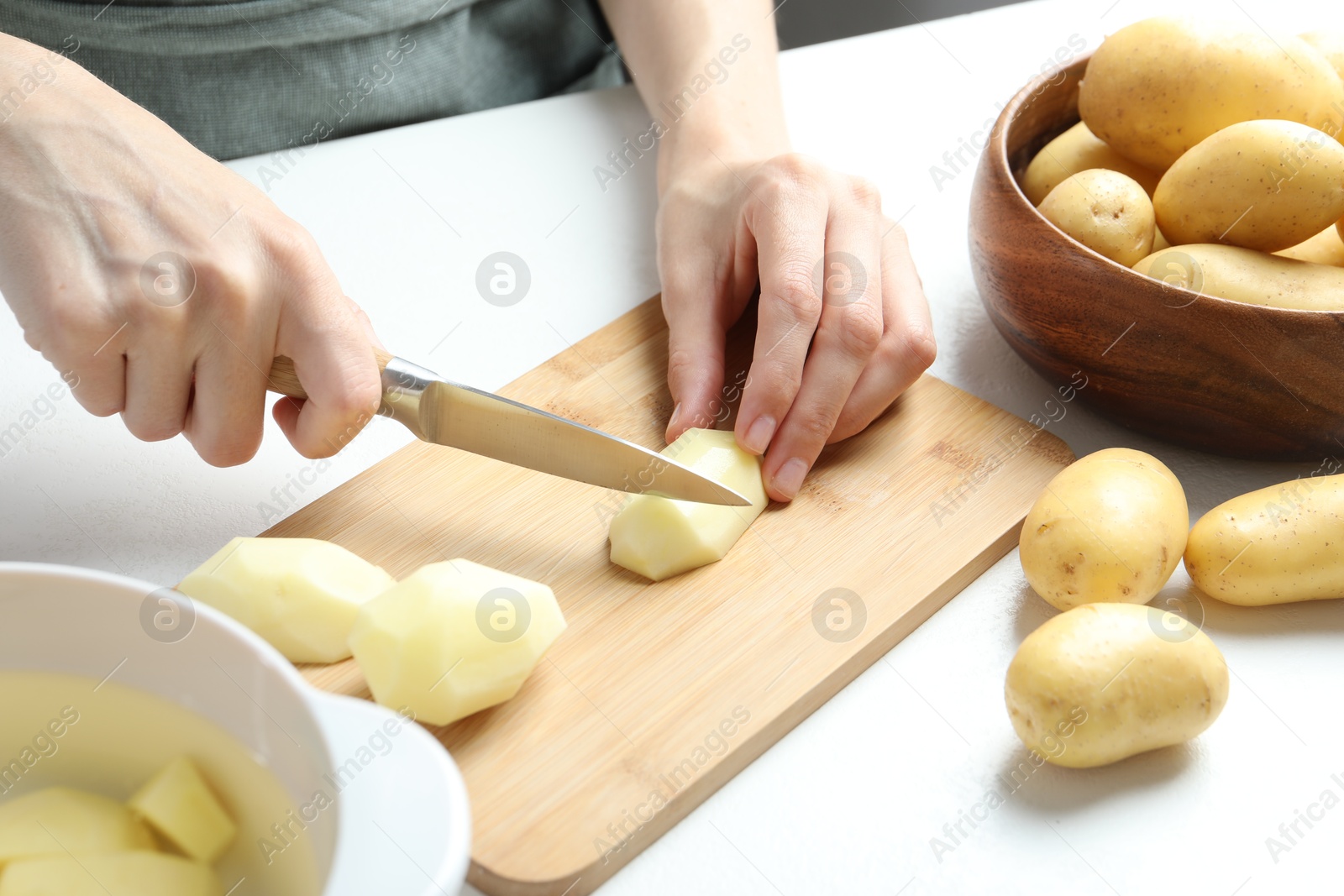 Photo of Woman cutting raw potato at white table, closeup