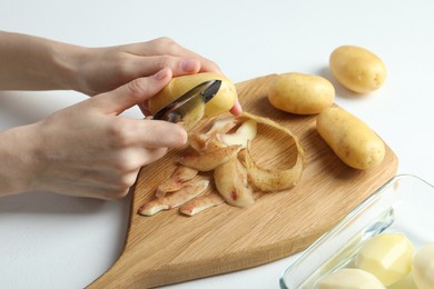 Photo of Woman peeling fresh potato with peeler at white table, closeup