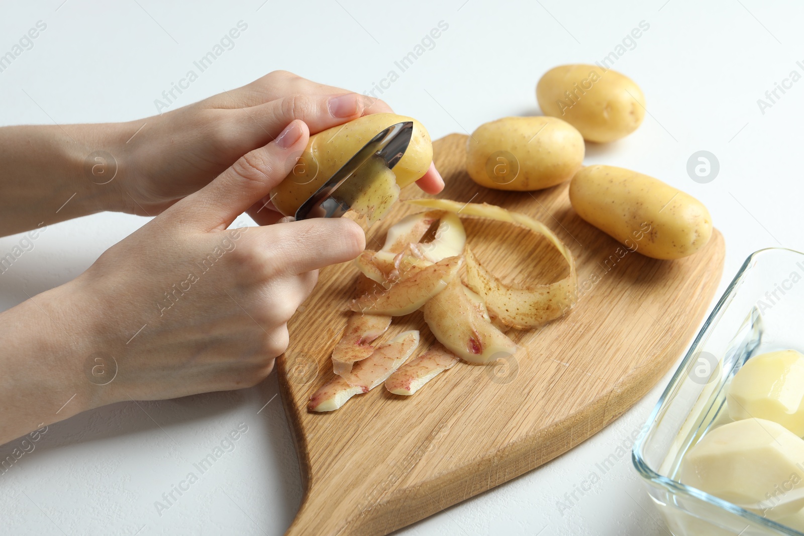 Photo of Woman peeling fresh potato with peeler at white table, closeup