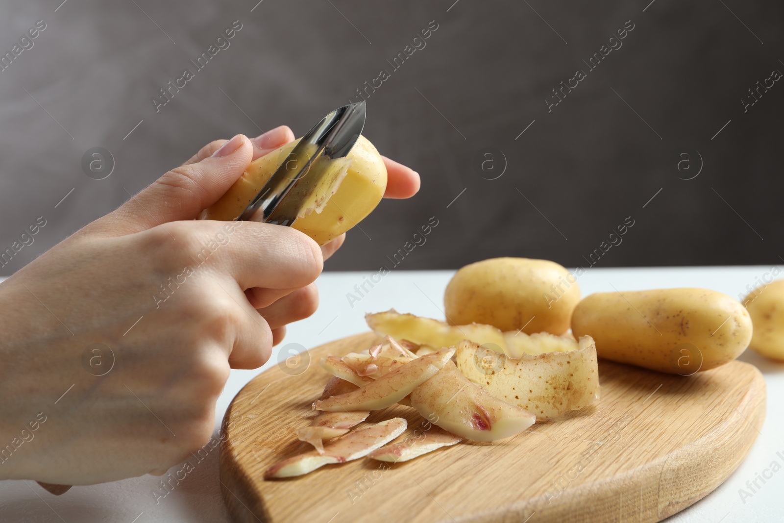 Photo of Woman peeling fresh potato with peeler at white table, closeup