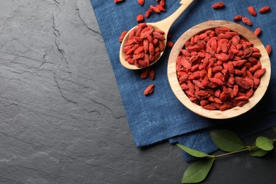 Dried goji berries and leaves on dark textured table, top view. Space for text