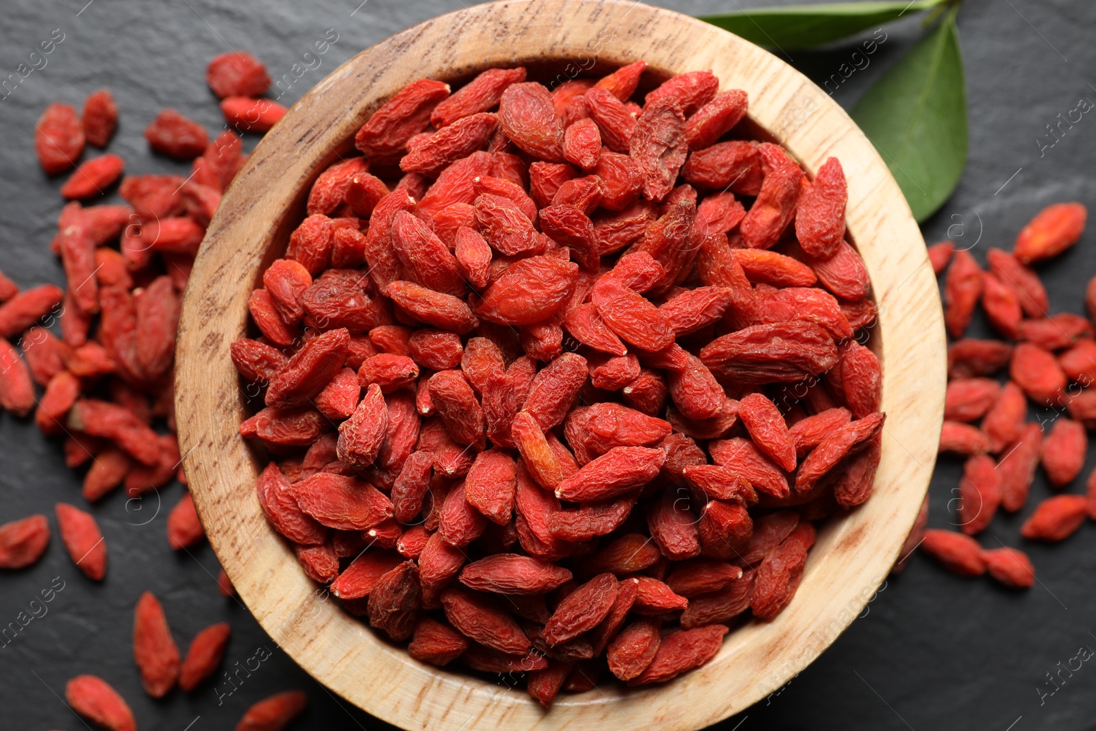 Photo of Dried goji berries in bowl on dark textured table, flat lay