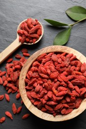 Dried goji berries and leaves on dark textured table, flat lay