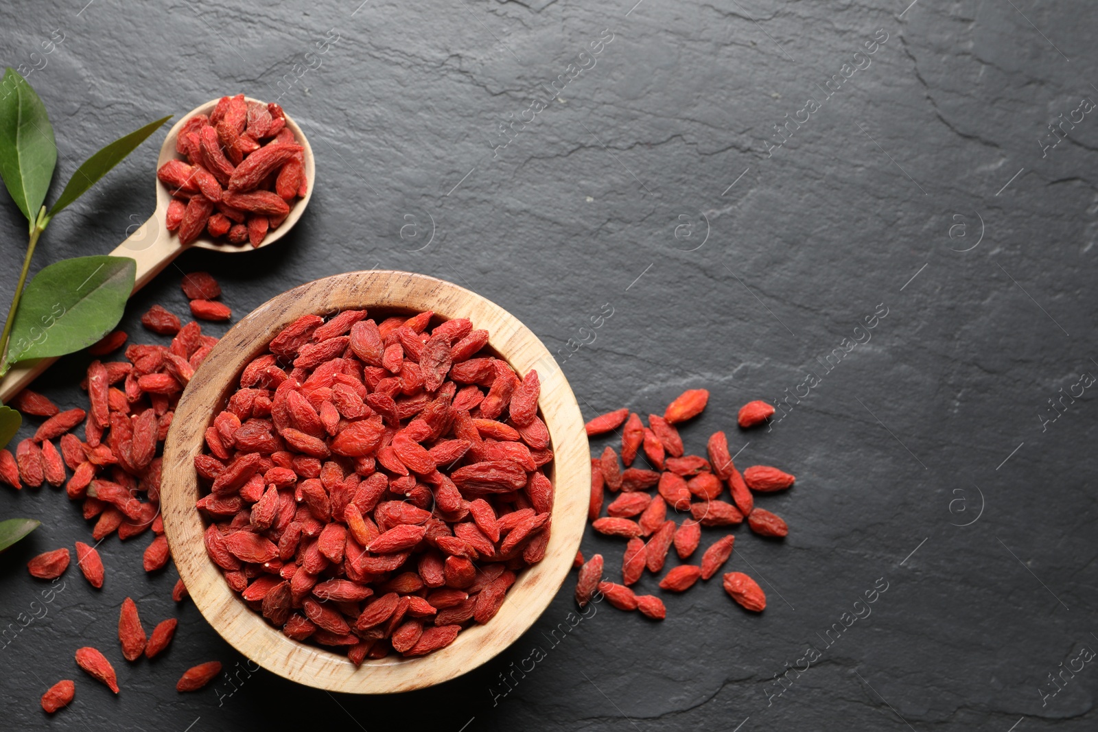 Photo of Dried goji berries and leaves on dark textured table, flat lay. Space for text