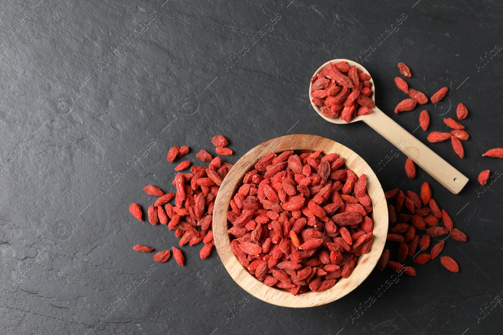 Photo of Dried goji berries on dark textured table, flat lay. Space for text