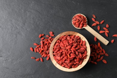 Photo of Dried goji berries on dark textured table, flat lay. Space for text