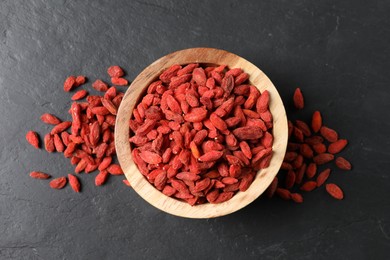 Photo of Dried goji berries in bowl on dark textured table, top view