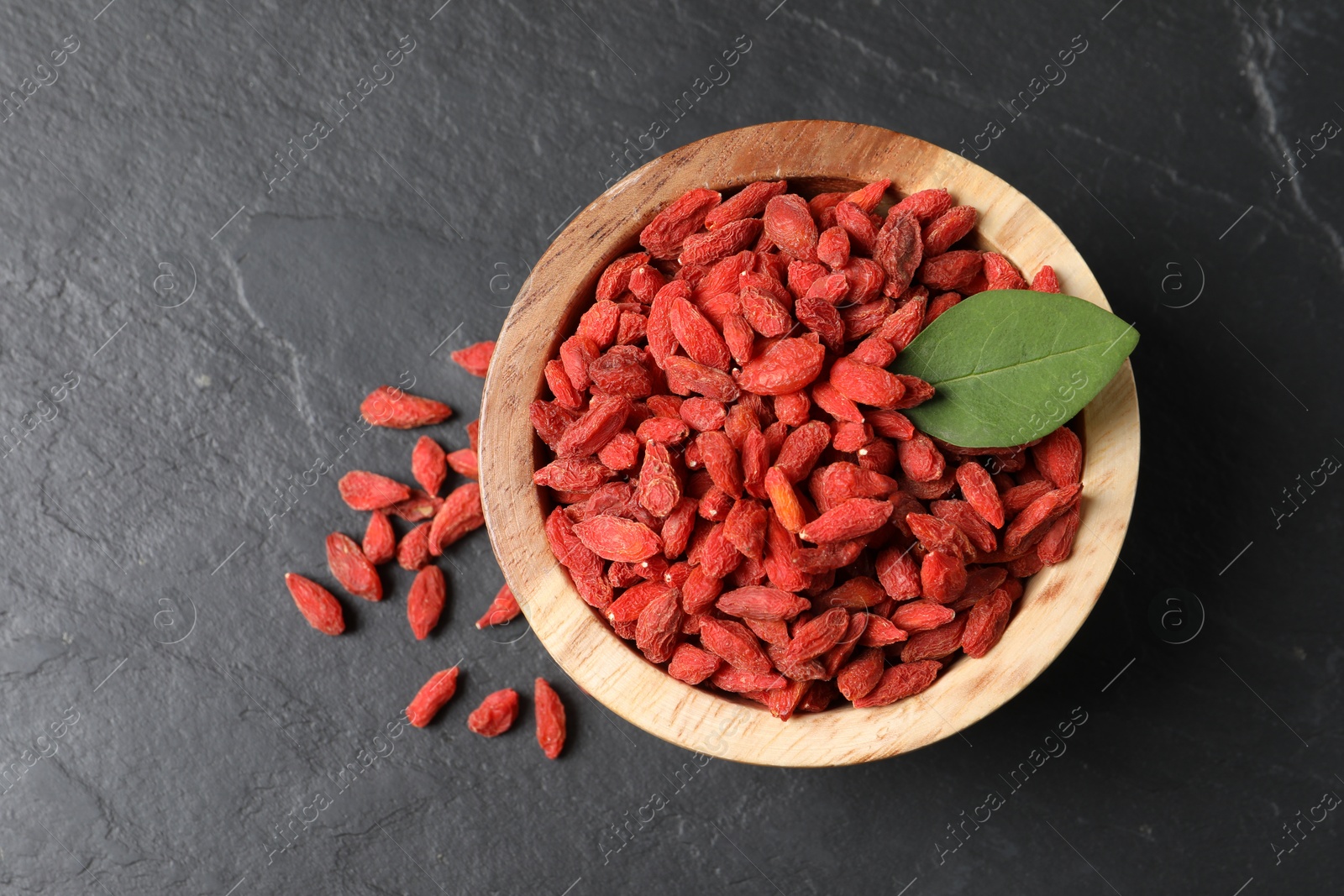 Photo of Dried goji berries in bowl on dark textured table, top view