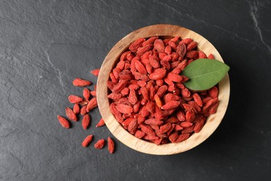 Photo of Dried goji berries in bowl on dark textured table, top view