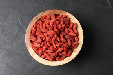 Dried goji berries in bowl on dark textured table, top view