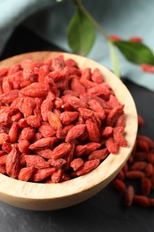 Photo of Dried goji berries in bowl on dark textured table, closeup