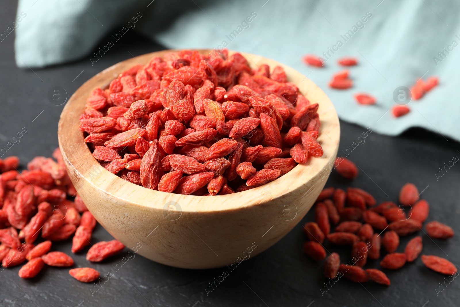 Photo of Dried goji berries in bowl on dark textured table, closeup