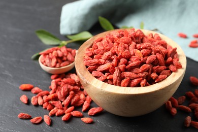 Photo of Dried goji berries in bowl on dark textured table, closeup