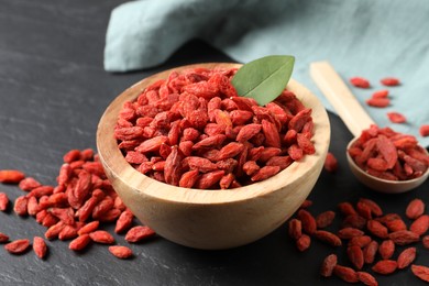 Photo of Dried goji berries in bowl on dark textured table, closeup