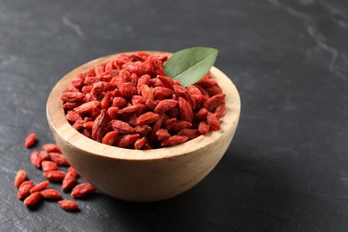 Photo of Dried goji berries in bowl on dark textured table, closeup