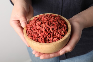 Woman holding bowl with dried goji berries on light background, closeup