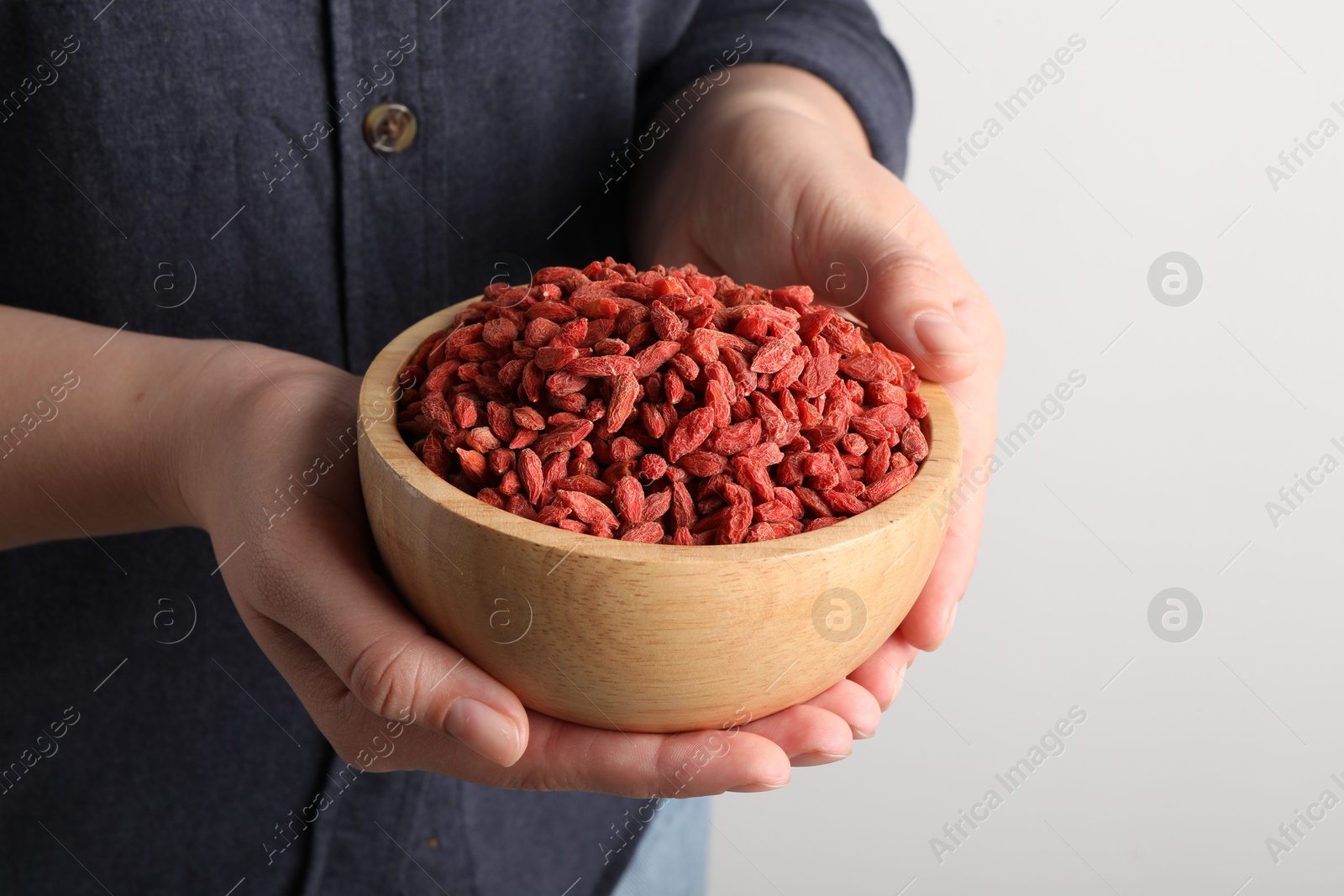 Photo of Woman holding bowl with dried goji berries on light background, closeup