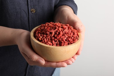 Photo of Woman holding bowl with dried goji berries on light background, closeup