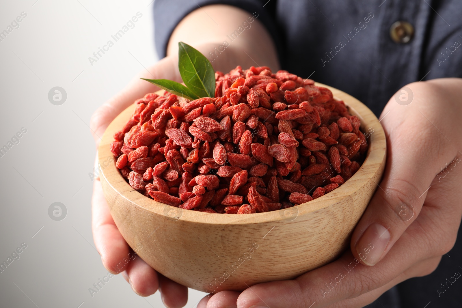 Photo of Woman holding bowl with dried goji berries on light background, closeup