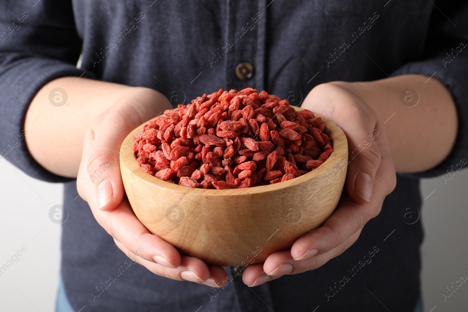 Photo of Woman holding bowl with dried goji berries on light background, closeup