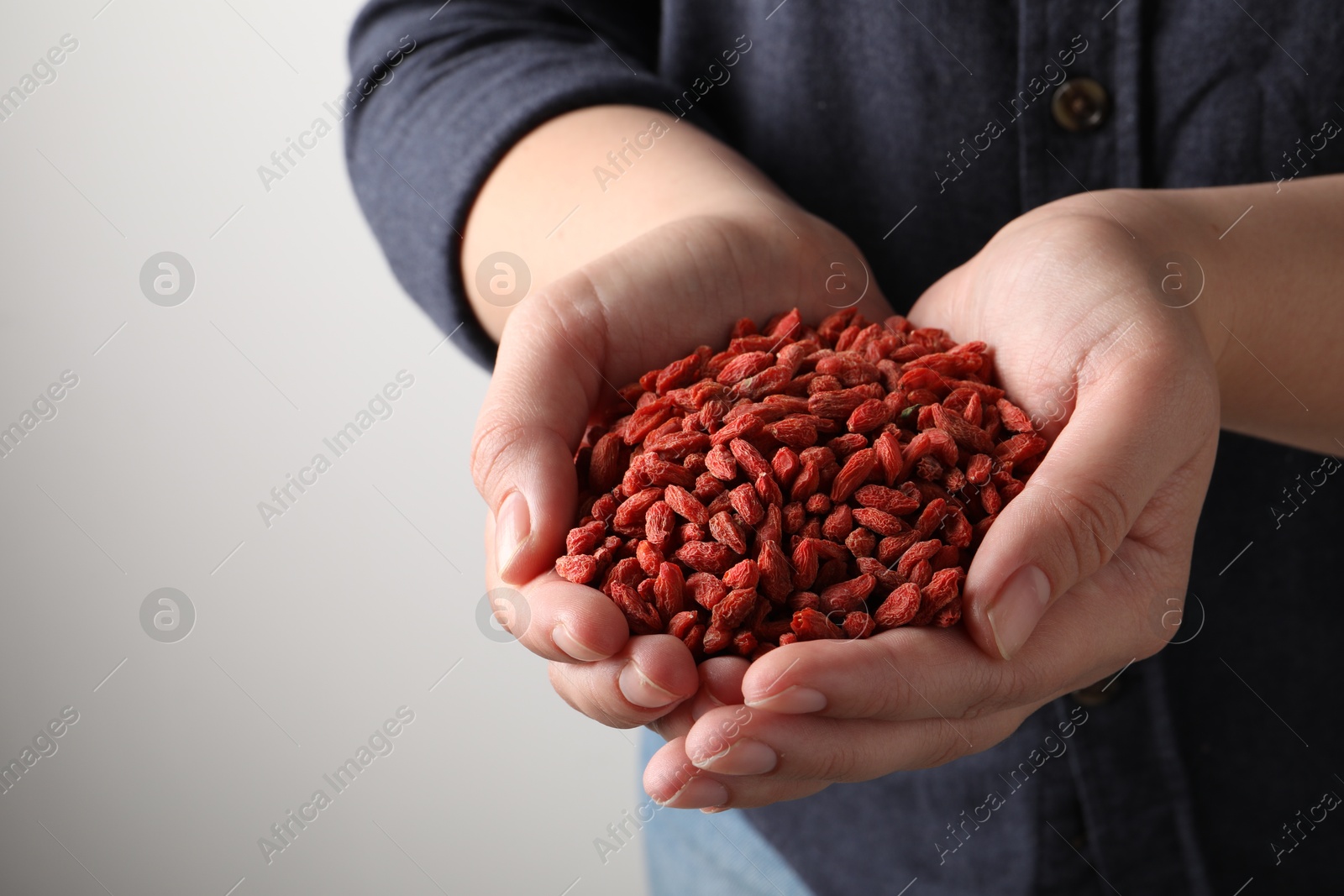 Photo of Woman holding pile of dried goji berries on grey background, closeup. Space for text